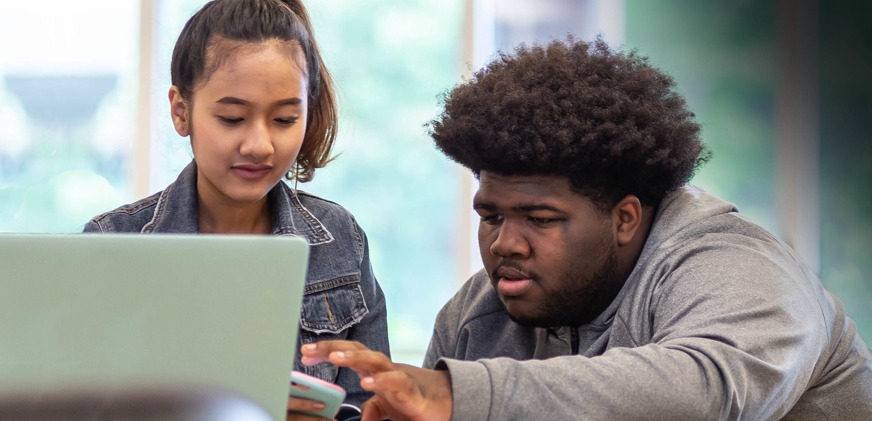  two students in a classroom setting with a laptop computer and cell phone 