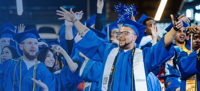 several smiling students in caps and gowns at commencement