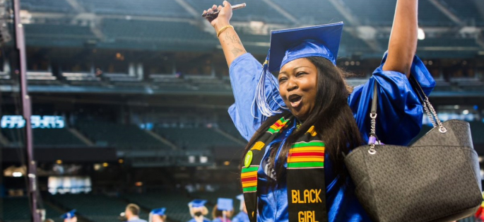 A student joyfully raising her arms after crossing the stage at commencement