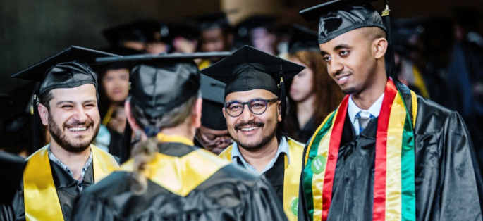 students in caps and gowns smiling and talking with each other