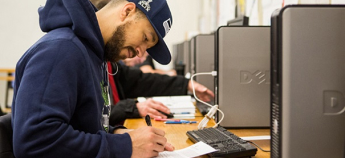 student writing in a notebook near a computer