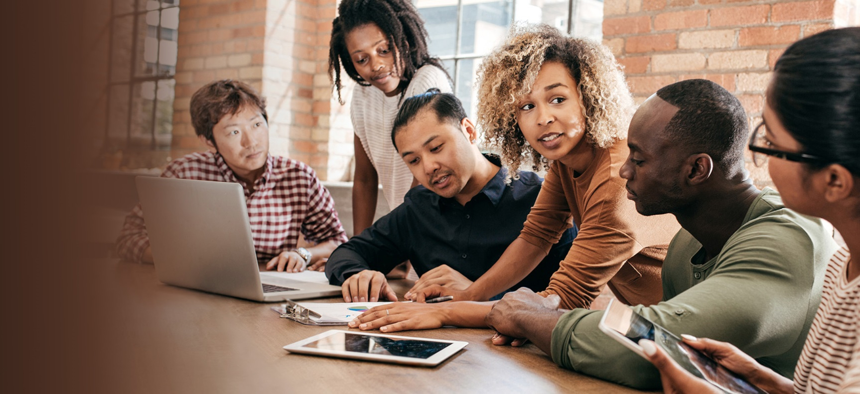 a diverse team of people talking at a table with computers