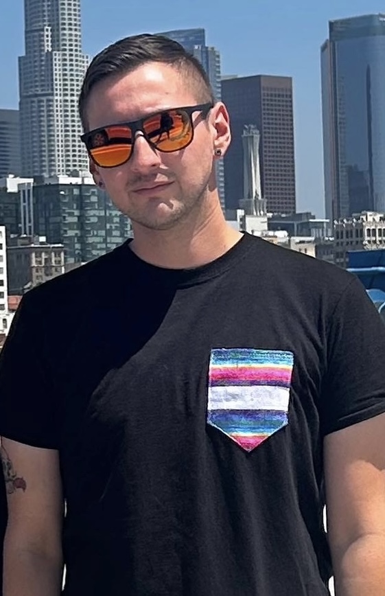 Julian standing outside with cityscape in background wearing sunglasses looking directly at camera.