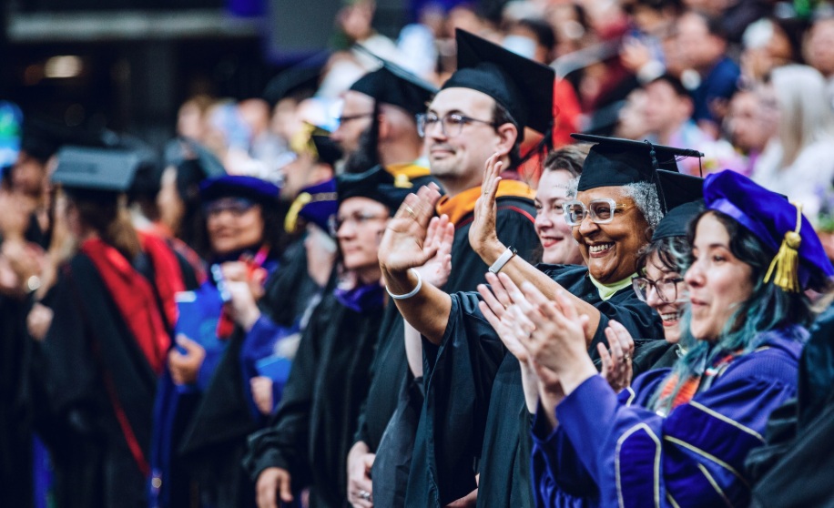 Smiling faculty and staff wearing academic regalia and participating in the processional at Commencement 2025