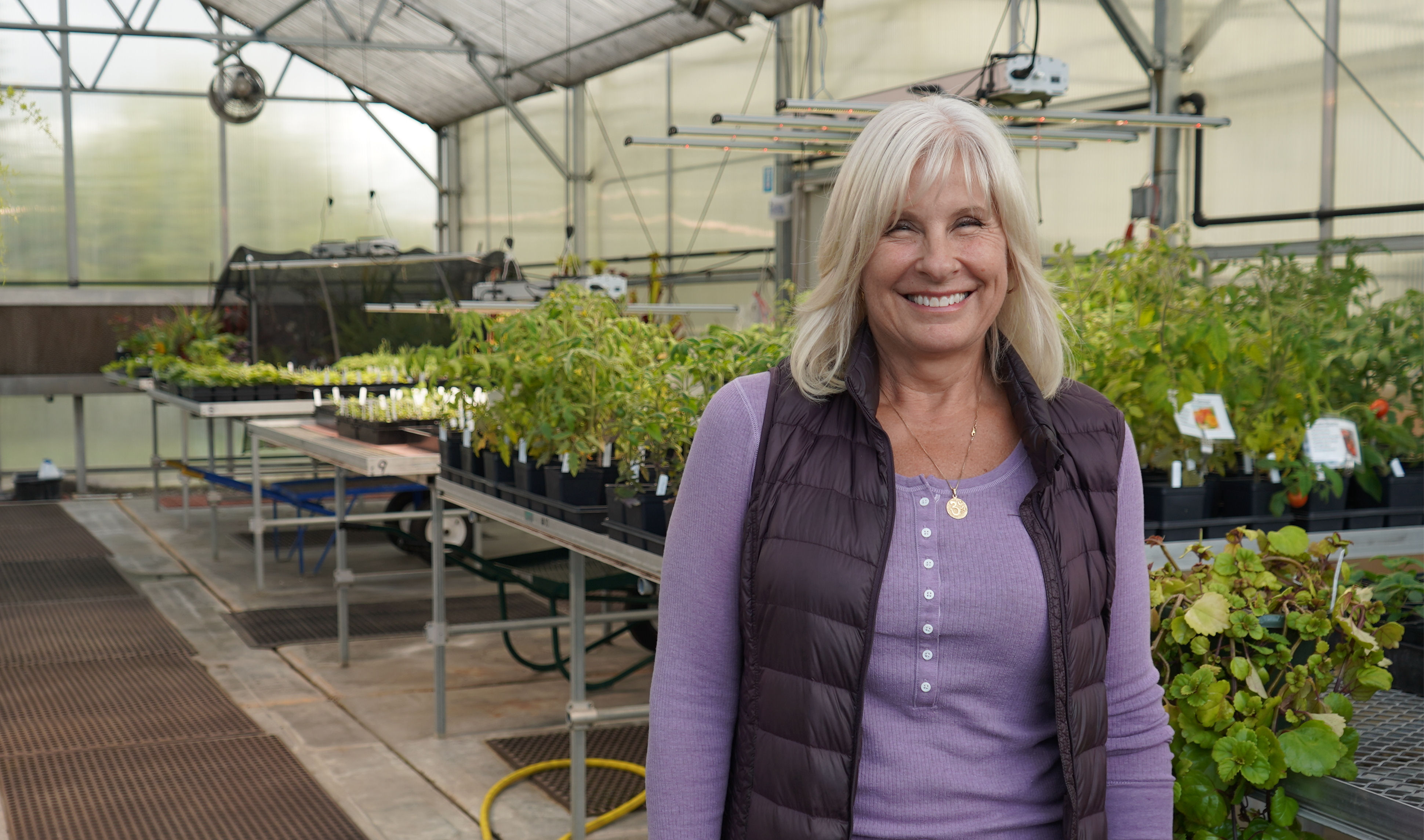 Shelly Hurst in a campus greenhouse surrounded by plants